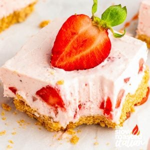 Close-up of a no bake strawberry cheesecake bar with graham cracker crust, creamy filling, and a fresh strawberry on top