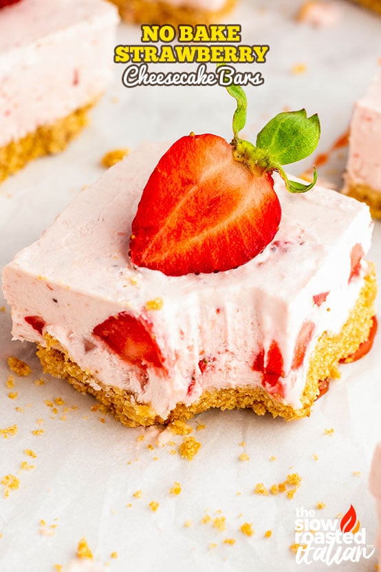 No bake strawberry cheesecake bars cut into squares on parchment, topped with fresh strawberries