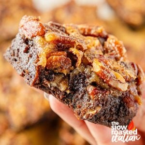 Hand holding a pecan pie brownie with a gooey pecan topping and fudgy chocolate layer underneath
