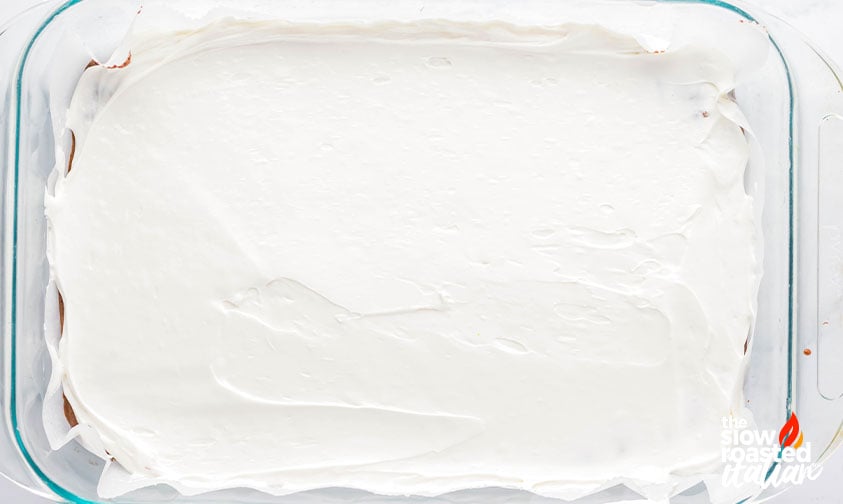 White marshmallow frosting spread over baked brownies in a pan for coconut brownies