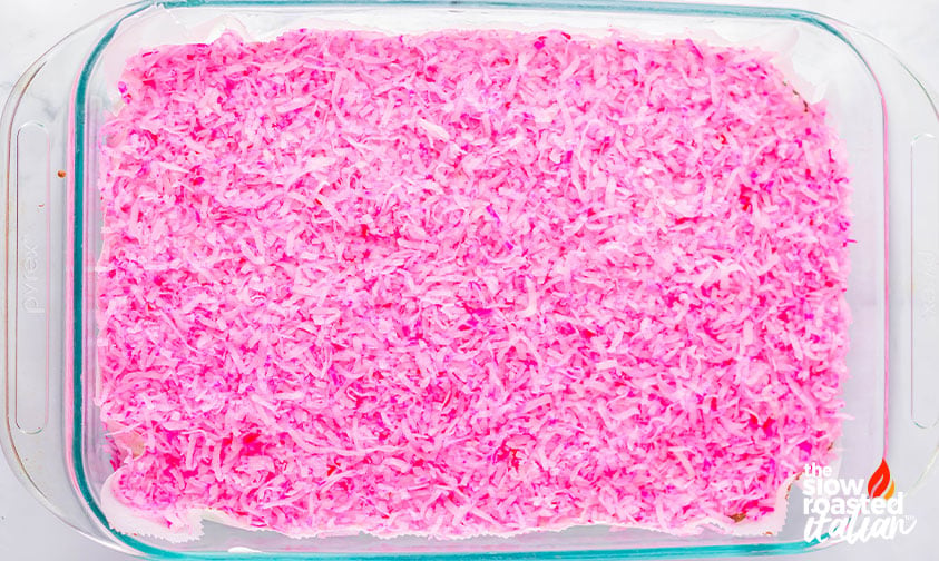 Pink shredded coconut sprinkled over frosted brownies in a pan for coconut brownies