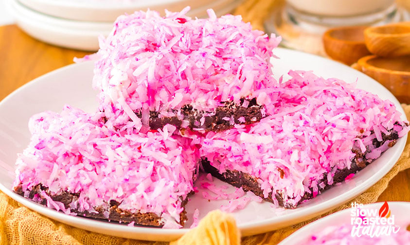 Stacked coconut brownies with pink shredded coconut topping and fudgy brownie base on a white plate