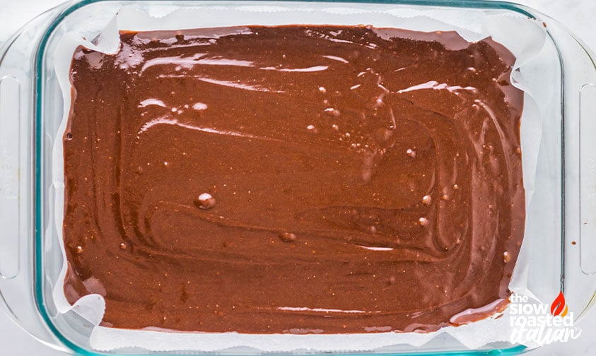 Brownie batter spread in a lined baking pan before baking coconut brownies