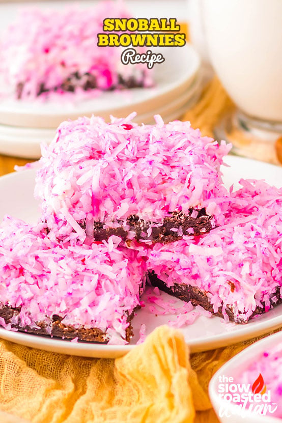 Coconut brownies topped with pink shredded coconut, stacked on a plate with a bite taken out showing the fudgy brownie layer
