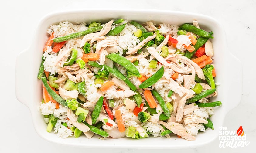 Shredded chicken, rice, and mixed vegetables layered in a casserole dish before baking teriyaki chicken casserole