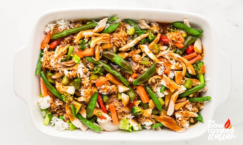 Teriyaki sauce poured over chicken, rice, and vegetables in a casserole dish before baking teriyaki chicken casserole