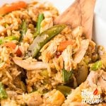 Close-up of teriyaki chicken casserole with shredded chicken, rice, snap peas, and carrots scooped with a wooden spoon