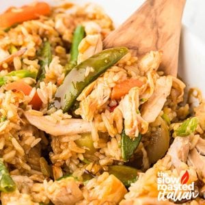 Close-up of teriyaki chicken casserole with shredded chicken, rice, snap peas, and carrots scooped with a wooden spoon