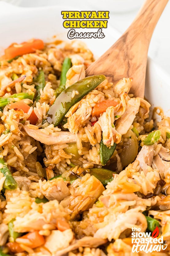 Close-up of teriyaki chicken casserole with rice, snap peas, carrots, and shredded chicken being scooped with a wooden spoon